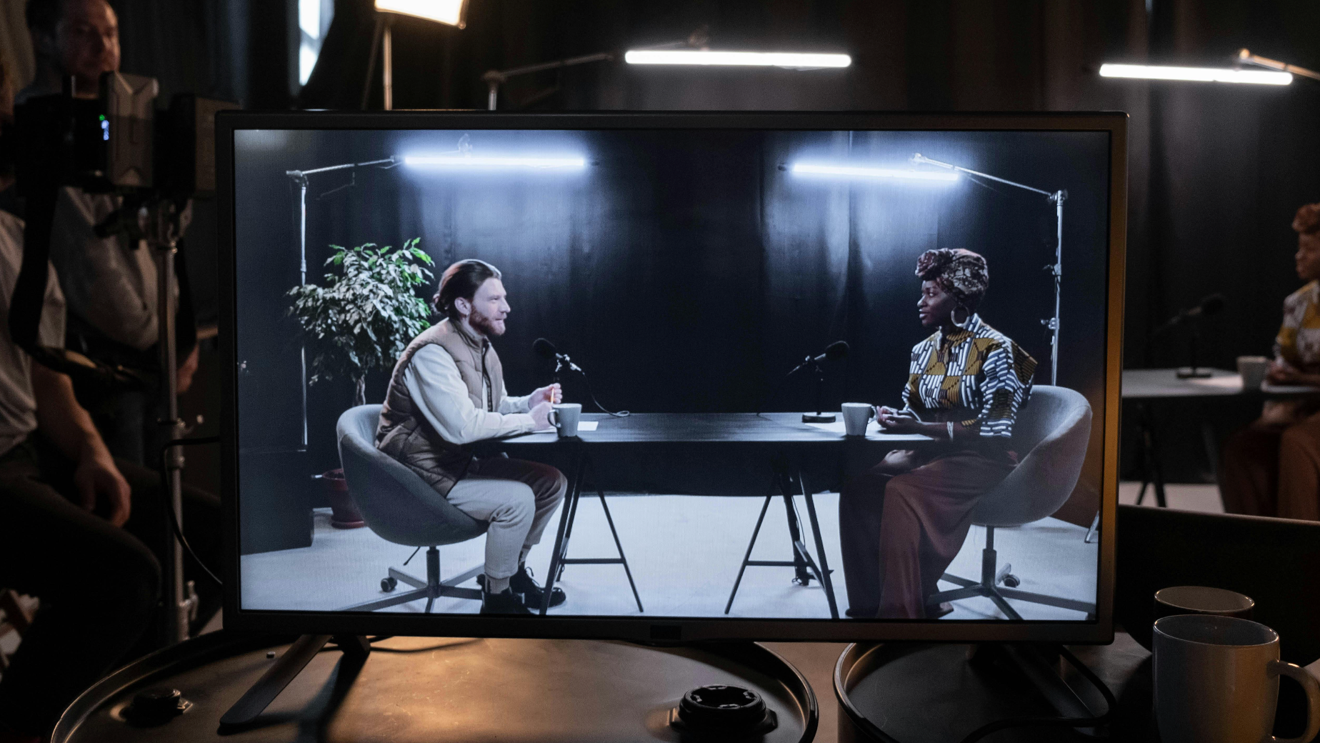 Studio setup with a monitor displaying a video call between two people, surrounded by filming equipment.